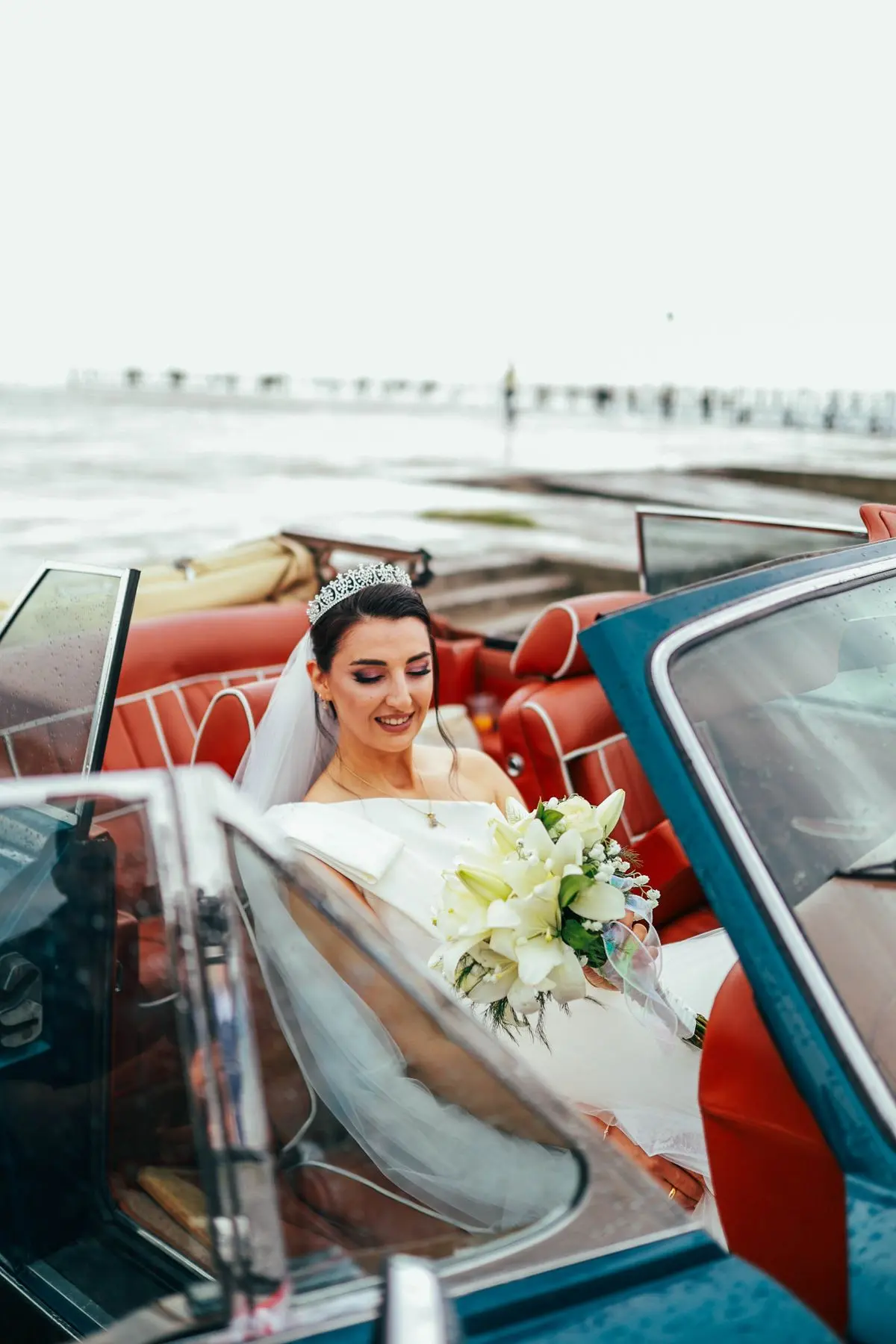 Bride in a wedding dress sitting in an open-top convertible holding her bouquet