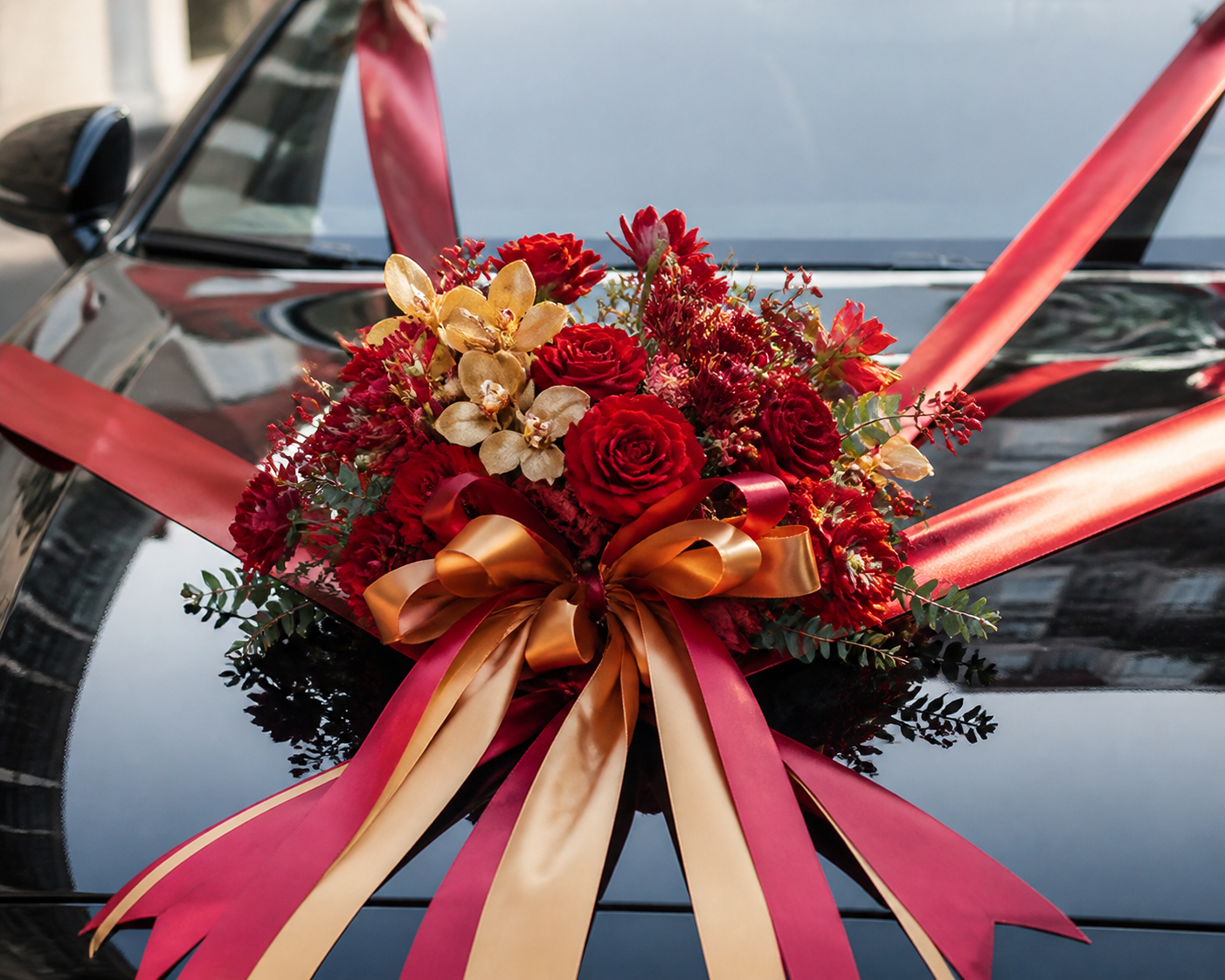 Red and gold Chinese bridal car decoration with red roses and satin ribbons on a dark car